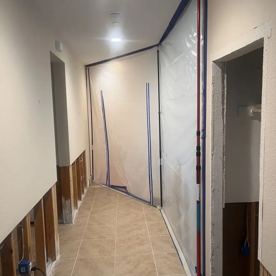 A hallway sealed with plastic containment and drywall cut along the bottom of the walls