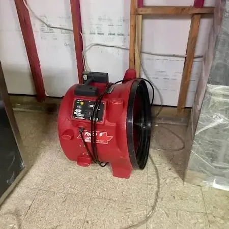 A red air mover drying a room where the lower wall was opened and plastic sheeting was hung