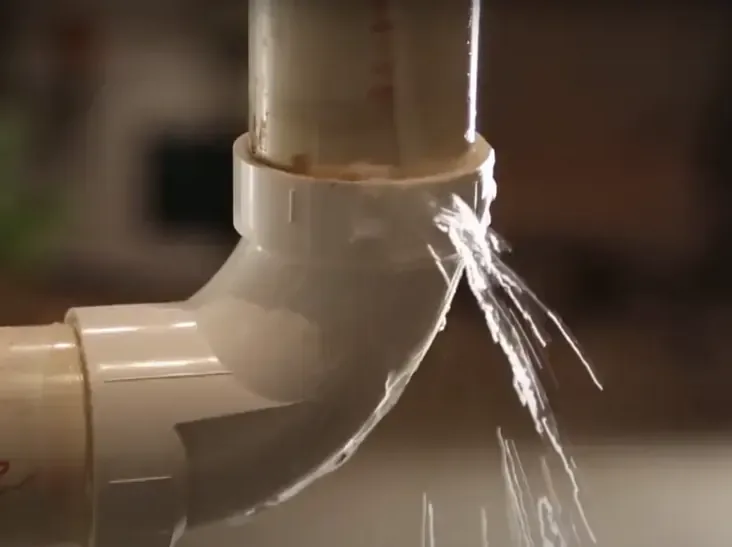 Water spraying from a cracked pipe fitting inside a house
