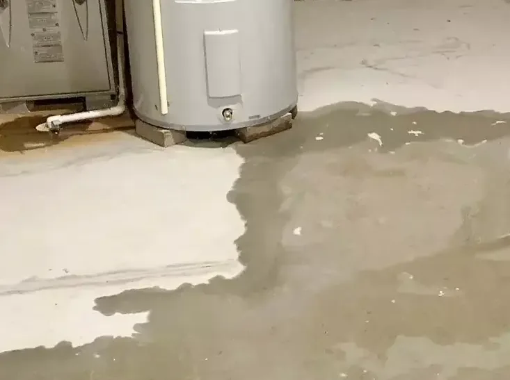 Water spreading across a concrete floor from the base of a leaking water heater